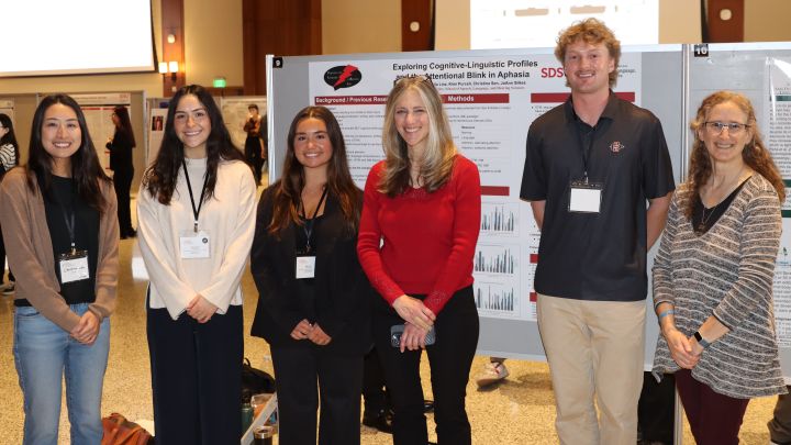 Dr. Bonomi in a red top standing with students infront of their research poster.